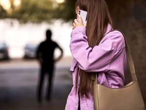 Woman holding mobile phone looking backwards to shadow of a man
