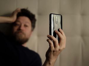 Out-of-focus man with his hand on his head looking at a cell phone screen he is holding