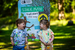Two children standing in front of a Stick Man trail panel in a forest