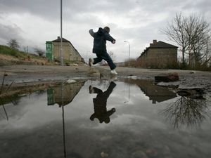A child leaps over a puddle on a poverty-stricken estate in Glasgow