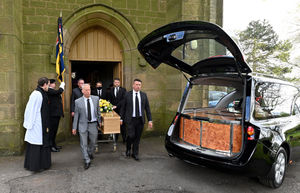 A standard bearer is present as the coffin leaves the church