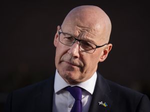 Headshot of John Swinney against a black background