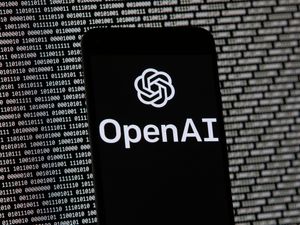 The OpenAI logo appears on a mobile phone in front of a computer screen with random binary data