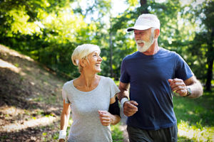 A senior man and woman smiling while running together.