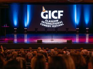 Audience looking at an empty stage, which features the words 'Glasgow International Comedy Festival' and a microphone