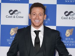 Joe Swash smiles in a suit and tie