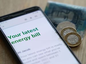 An energy bill displayed on a mobile phone alongside a five pound note and loose change
