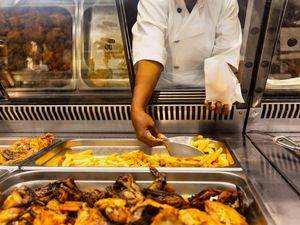 A shop worker scooping up chips and fried chicken