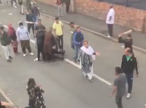 A bat is raised towards a man's head as he faces the other direction. Video: Khan Hussain/YouTube