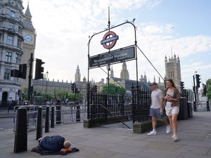 A homeless person asleep on the street near an entrance to Westminster Underground station and the Houses of Parliament