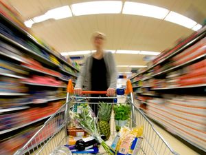 A woman pushing a shopping trolley in a supermarket aisle
