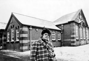 nostalgia pic. Tipton. Mrs Annie Clarkson returning to her old school at Tipton in February 1976. This is a print in the Express and Star picture library (in the basement archive at Queen Street, and copied in situ on Tuesday, May 18, 2021). The story pasted on the back reads: 'Tipton was a place of fields and market gardens when widow Annie Clarkson was a girl. For more than 50 years she cherished memories of returning to the school where she spent some of the happiest days of her life. But the reality of the situation shattered her dreams, Mrs Clarkson said today. As a girl the then Annie Fagan was among the first scholars to attend the newly-built Princes End Joint Schools. And she nursed a desire to make one last visit to the haunts of her childhood. 'Now I wish I hadn't. The buildings looked horrible, surrounded by sheds like pigeon lofts. I was very disillusioned,\ said Mrs Clarkson, who lives at St Joseph's Court, Merry Hill, Wolverhampton. She is pictured outside the school. 'I could have cried when I visited the old school. When I was a pupil there the school was surrounded by fields and market gardens. We loved going to school.'\ The print has a datestamp of February 4, 1976, which is probably publication date. It has the Express and Star copyright stamp. The photographer's name is not recorded. Tipton school. The school was in Tibbington Terrace and closed in 2005. Library code: Tipton nostalgia 2021.