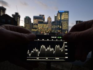 A person views share prices on an iPhone, with London’s Canary Wharf in the background