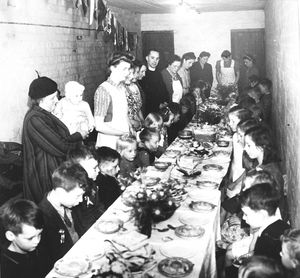 A 'victory party' for children from Pope Road in an air raid shelter in a churchyard. The photograph shows the Reverend H. S. Light, minister of Low Hill Congregational Church, saying grace before the feast in 1945.