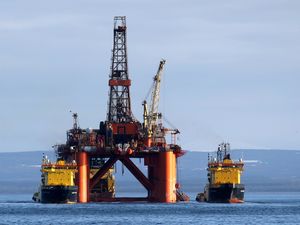 An oil rig at sea, with two ships alongside it