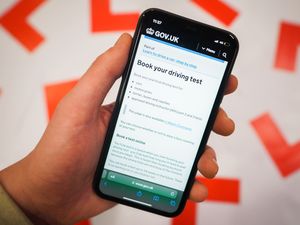 A driving test page on the gov.uk website shown on a phone next to driving L plates