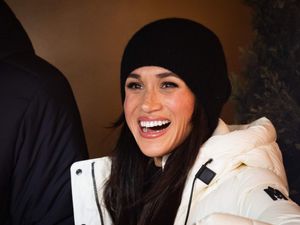 A smiling woman in a black beanie hat and a white coat