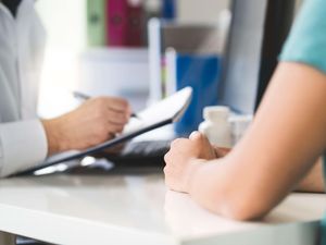 A doctor sitting at a table using a pen and notepad in front of a patient