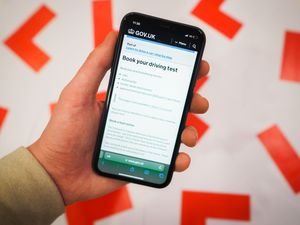 A driving test page on the gov.uk website shown on a phone next to driving L plates