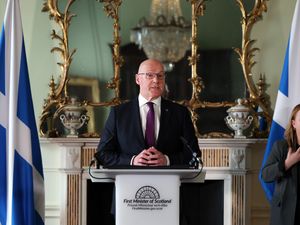 John Swinney standing behind a podium