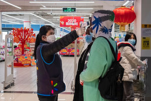A worker takes the temperature of a customer at the entrance of a Walmart store in Wuhan in central China's Hubei Province
