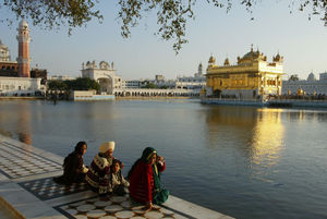 Pilgrims sit at the edge of the moat surrounding the Golden Temple of Amritsar