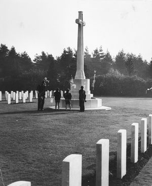 Cross of Sacrifice, Cannock Chase Military Cemetery. This photograph shows the Cross of Sacrifice, surrounded by headstones, with a man and three boys standing near the cross and looking up at it on November 8, 1959. A wreath is visible on the base of the cross. The cemetery is maintained by the Commonwealth War Graves Commission (CWGC).