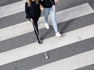 Two women on a zebra crossing, with one using a white stick