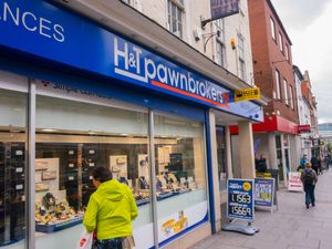A woman looking in the window of an H&T Pawnbrokers shop
