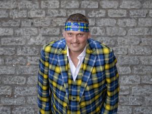 Doddie Weir dressed in a tartan suit and wearing a tartan headband, smiling at the camera