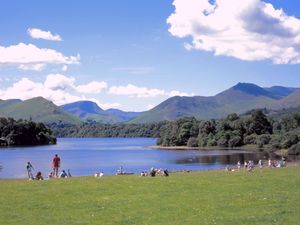 People sit on the grass by Derwent Water with Lake District hills in the background