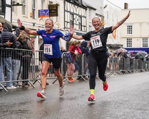 Two runners link arms as they approach the finish of last year's race, looking happy and relieved.