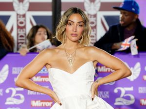 Frankie Bridge in a white dress with her hands on her hips