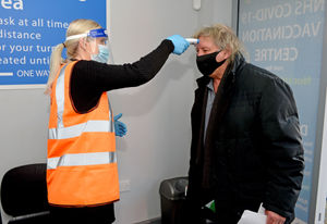 A man heading for his vaccination at Nucare Pharmacy has his temperature checked before entering