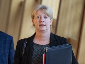 Shona Robison walking through a corridor at Holyrood, holding a black folder