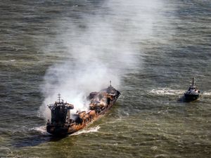 View from above of the Solong in the sea smoking, with a tug off its starboard side