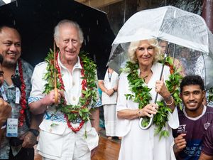 The King and Queen smile as they shelter under umbrellas while standing with members of the Apia rugby team during a visit to the Samoan Cultural Village in Apia.