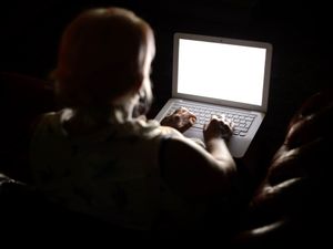 A view from behind of a woman working on a laptop in a darkened room