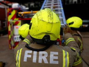 The back of a firefighter at the bottom of a ladder attached to a fire engine
