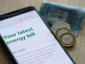 Energy bill displayed on a smart phone, with coins and banknotes beside it