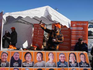 A member of Naleraq party attends a video call outside a polling station in Nuuk, Greenland, next to photos of parliamentary candidates