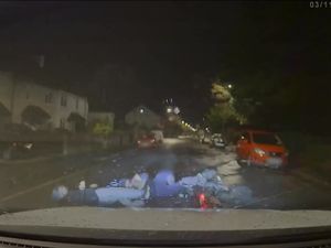 A video screen grab shows the moment a marked police car knocks the rider and pillion passenger off an electric motorbike