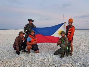 Philippine inter-agency members hold the Philippine flag as they visit Sandy Cay in the South China Sea