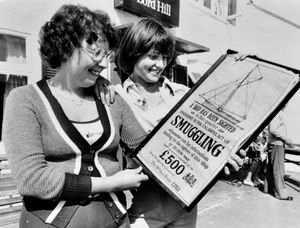 August 29, 1977, the caption pasted on the back reads: 'No smuggling at the inn... Miss Deborah Lloyd, left, and Miss Debbie Jarvis, of Broseley, view this unusual poster on display at the Lord Hill Inn, Broseley, this week.' The poster is dated October 19, 1782, and offers a reward for the capture of smugglers. 