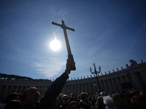 A cross is held aloft in the sunshine in St Peter’s Square