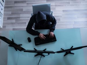 A man in a hoodie in front of several computer monitors