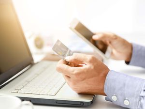 A man holding a bank card and mobile phone while using a laptop