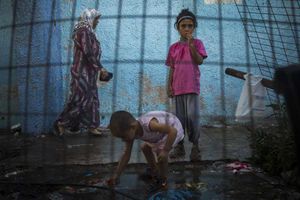 A girl takes water from a hose in Lesbos while waiting with her family to board a ferry to Athens