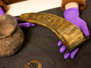 Gloved hands holding a horn-shaped item, next to a pot